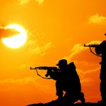 Silhouette shot of soldier holding gun with colorful sky and mountain in background